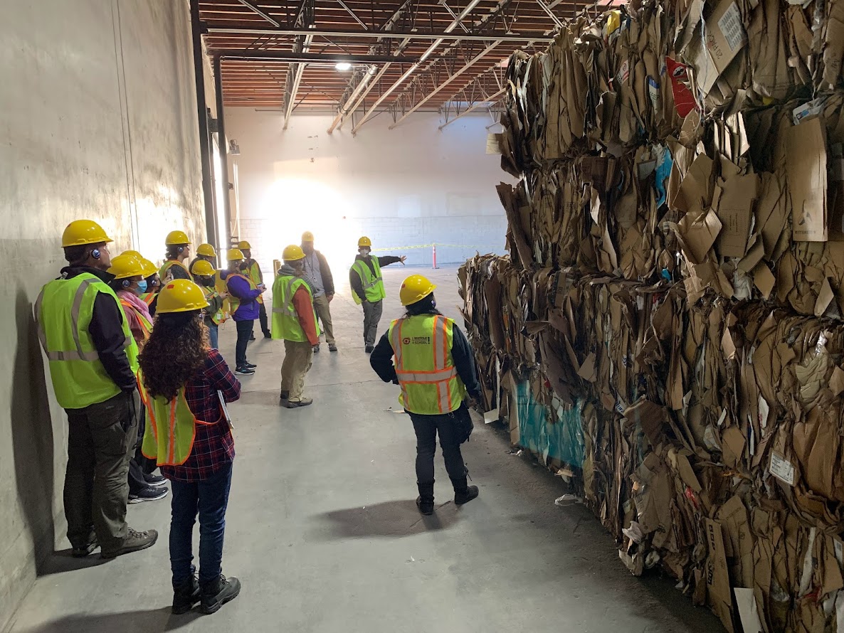 adults in hard hats next to towers of cardboard